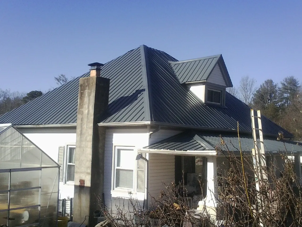 Dark blue standing seam metal roof on a white farmhouse with dormer — Slate & Tile Roof Repair by Roofing Brothers in Belews Creek