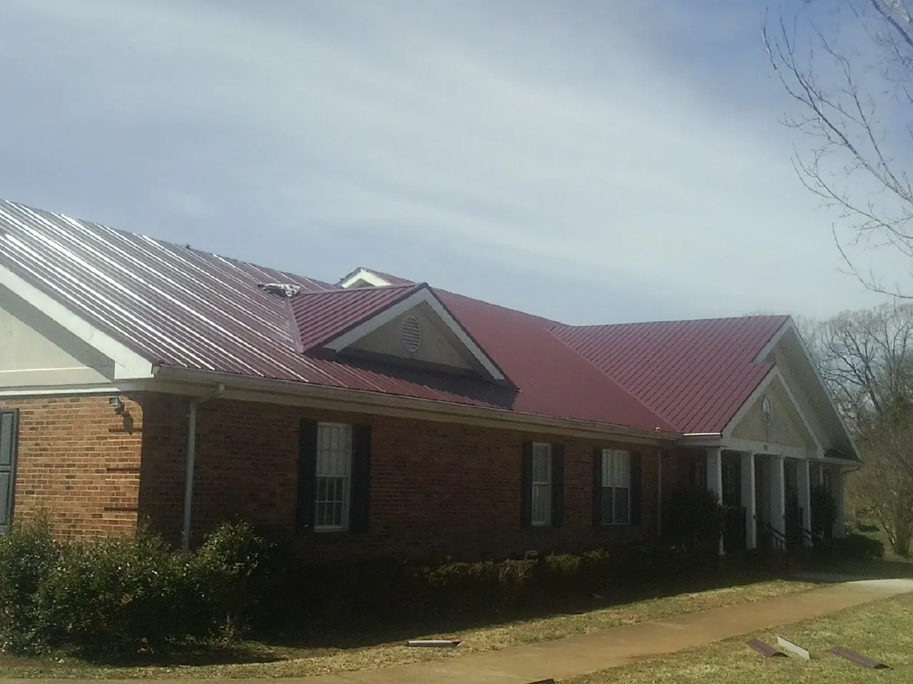 Red metal roof with gabled entries on a long brick building, from a Hail Damage Roof Repair job in Belews Creek