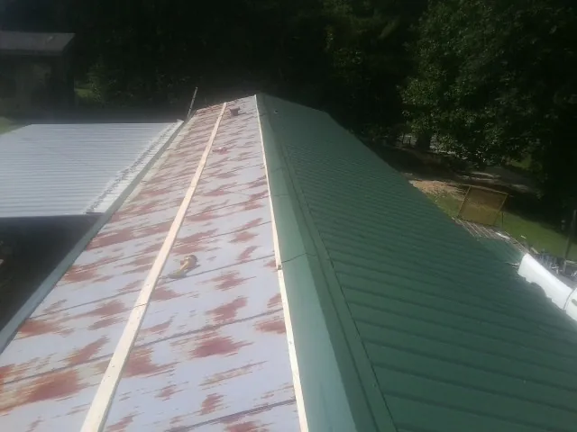 Old rusted panels beside newly installed green metal roofing — Wind Damage Roof Repair by Roofing Brothers in Belews Creek