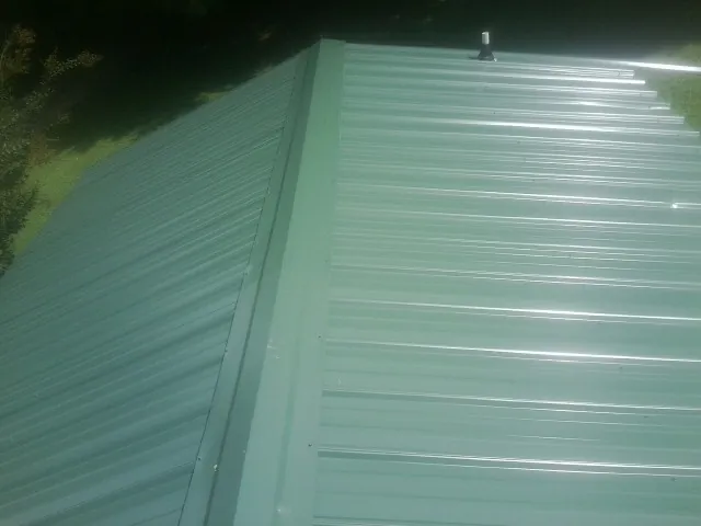 New green metal panels meeting at the ridge of a roof — Flat Roof Repair work by our crew in Belews Creek