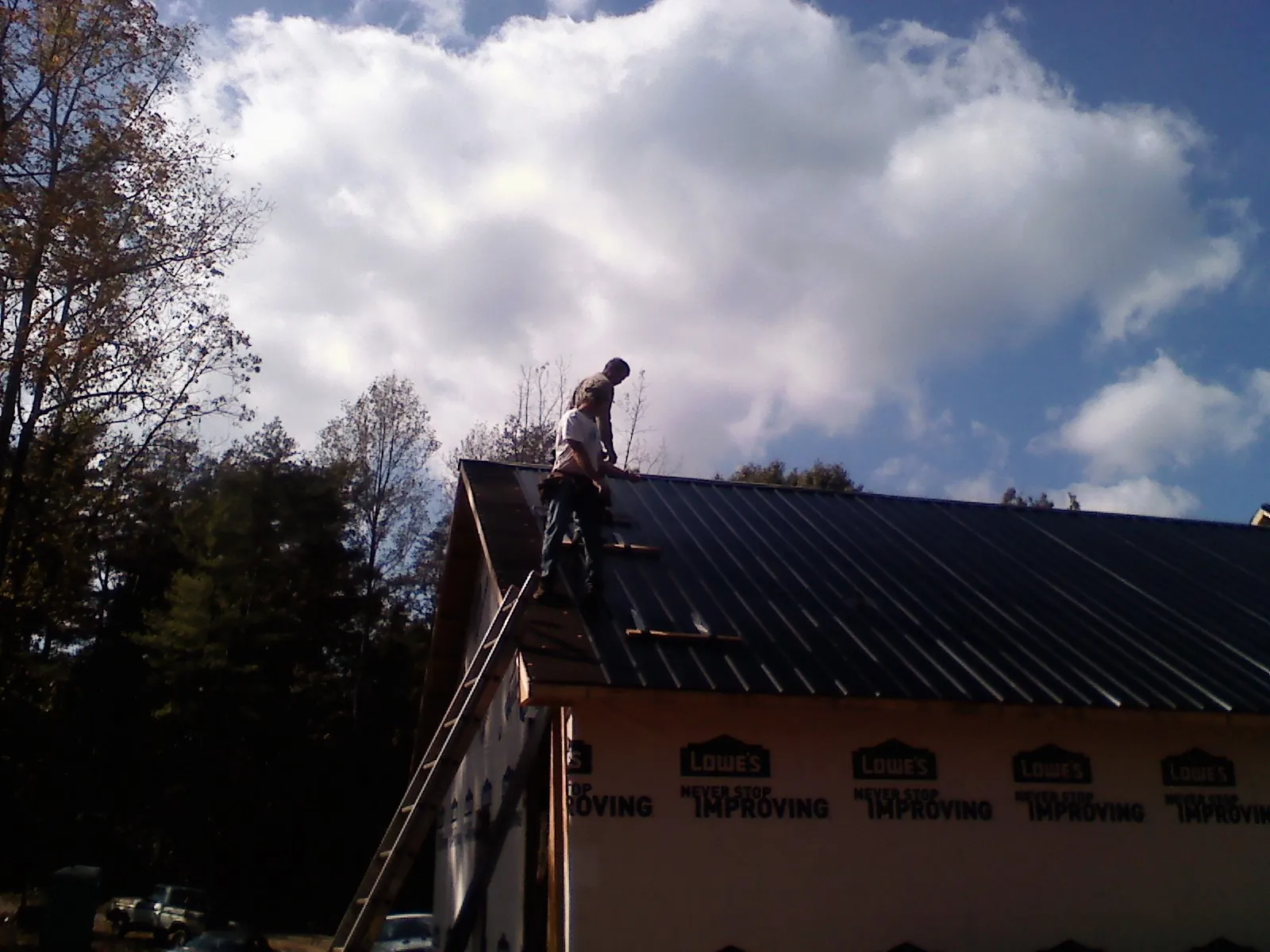 Roofer fastening dark metal panels high against a cloudy sky, from a Roof Inspection job in Belews Creek