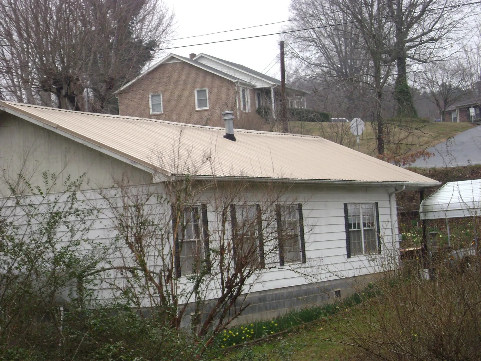 Tan metal roof on a white sided house set into a hillside — Commercial Roofing by Roofing Brothers in Belews Creek