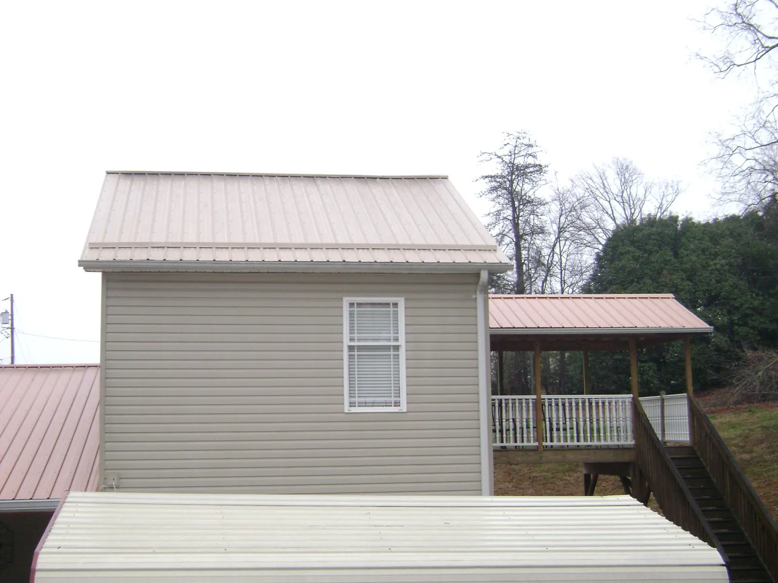 Tan metal roofs on a two story addition and attached porch, from a Roof Replacement job in Belews Creek