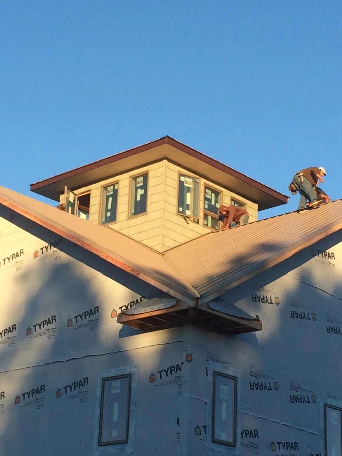 Roofers working around a rooftop cupola on a new metal roof at sunset — Roof Waterproofing in Belews Creek by Roofing Brothers
